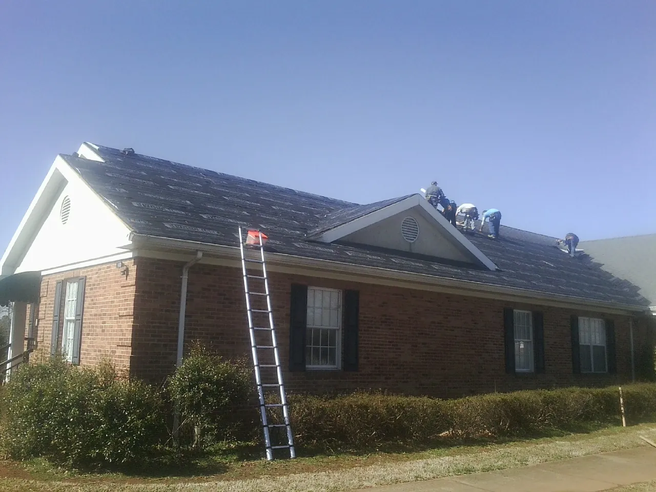 Crew tearing shingles off a brick ranch roof with a ladder set — Metal Roof Repair work by our crew in Stanhope