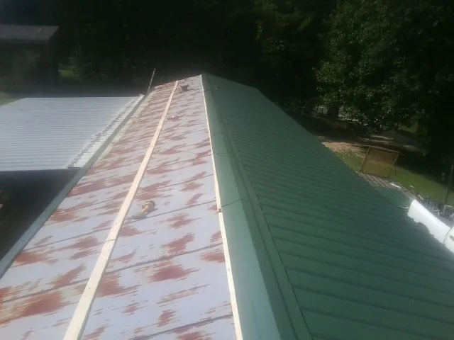 Old rusted panels beside newly installed green metal roofing — Wind Damage Roof Repair by Roofing Brothers in Stanhope