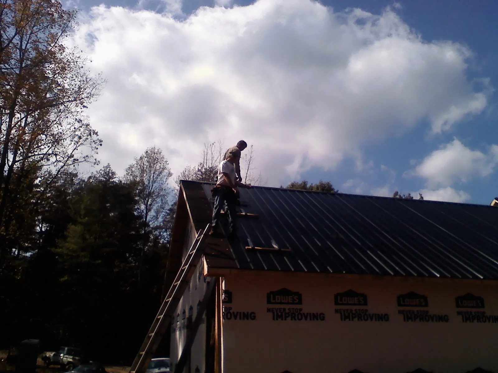 Roofer fastening dark metal panels high against a cloudy sky, from a Roof Inspection job in Stanhope