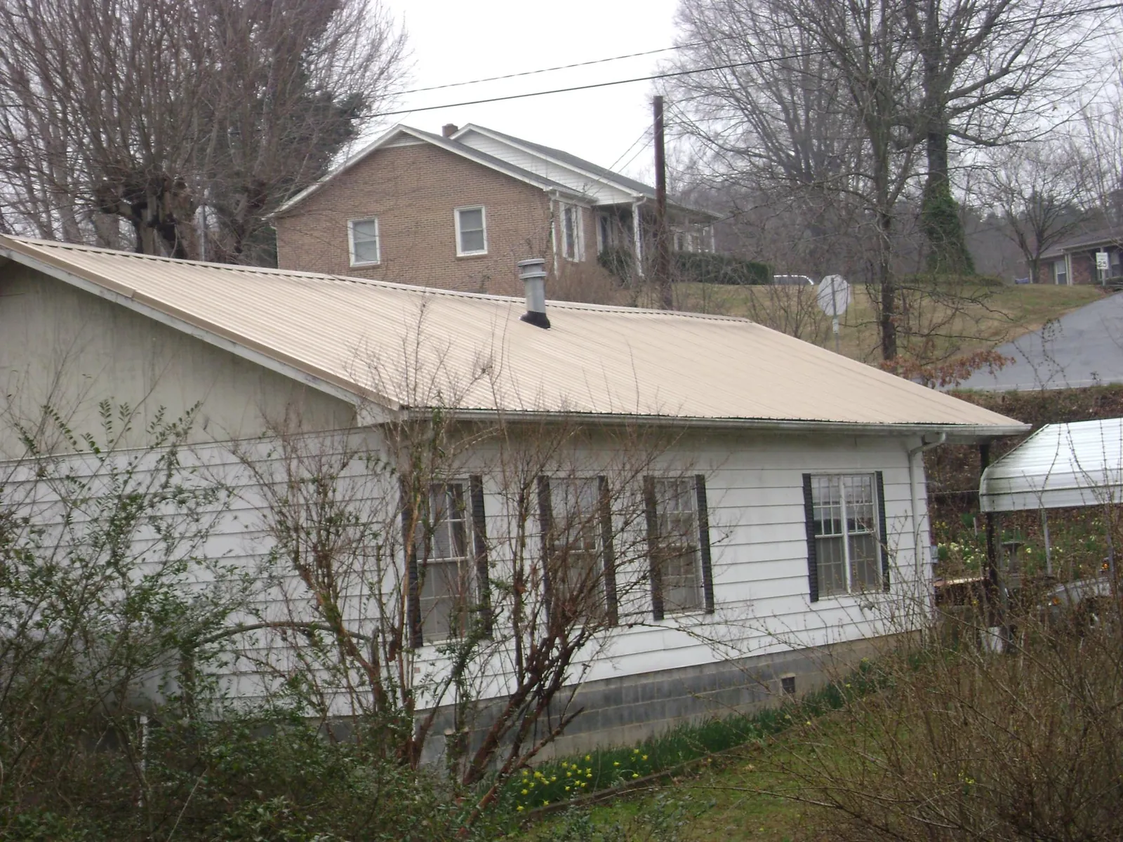 Tan metal roof on a white sided house set into a hillside — Commercial Roofing by Roofing Brothers in Stanhope