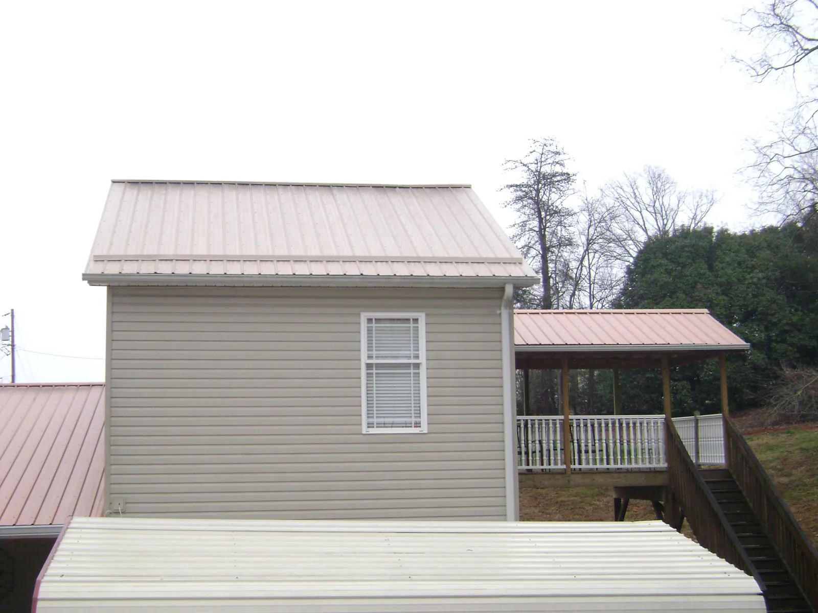Tan metal roofs on a two story addition and attached porch, from a Roof Replacement job in Stanhope